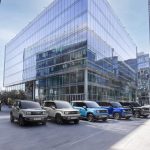 Linha de SUVs Chevrolet estacionados em frente a um moderno prédio comercial espelhado.