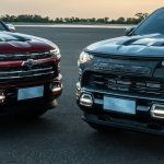 Frente de duas picapes Chevrolet modernas, estacionadas lado a lado em uma pista de asfalto ao entardecer.
