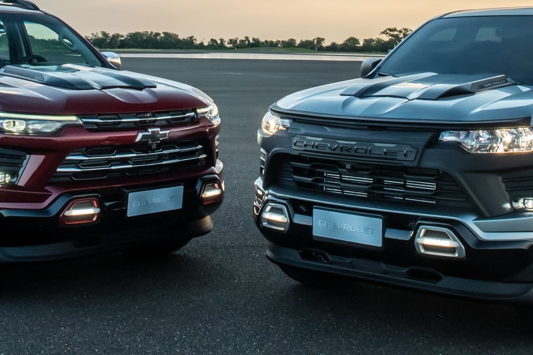 Frente de duas picapes Chevrolet modernas, estacionadas lado a lado em uma pista de asfalto ao entardecer.