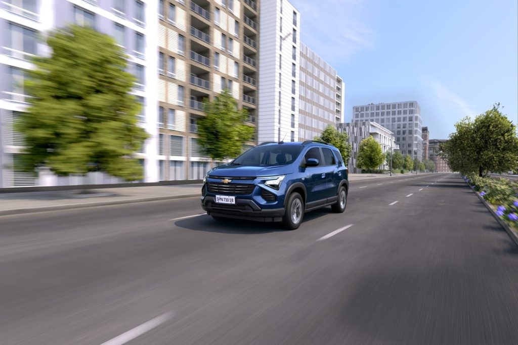 Chevrolet Spin azul em movimento em uma avenida urbana com prédios modernos ao fundo.