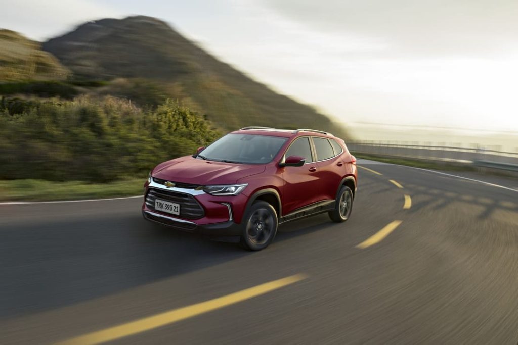 SUV Chevrolet Tracker vermelho percorrendo uma estrada sinuosa ao lado de uma montanha ao entardecer.