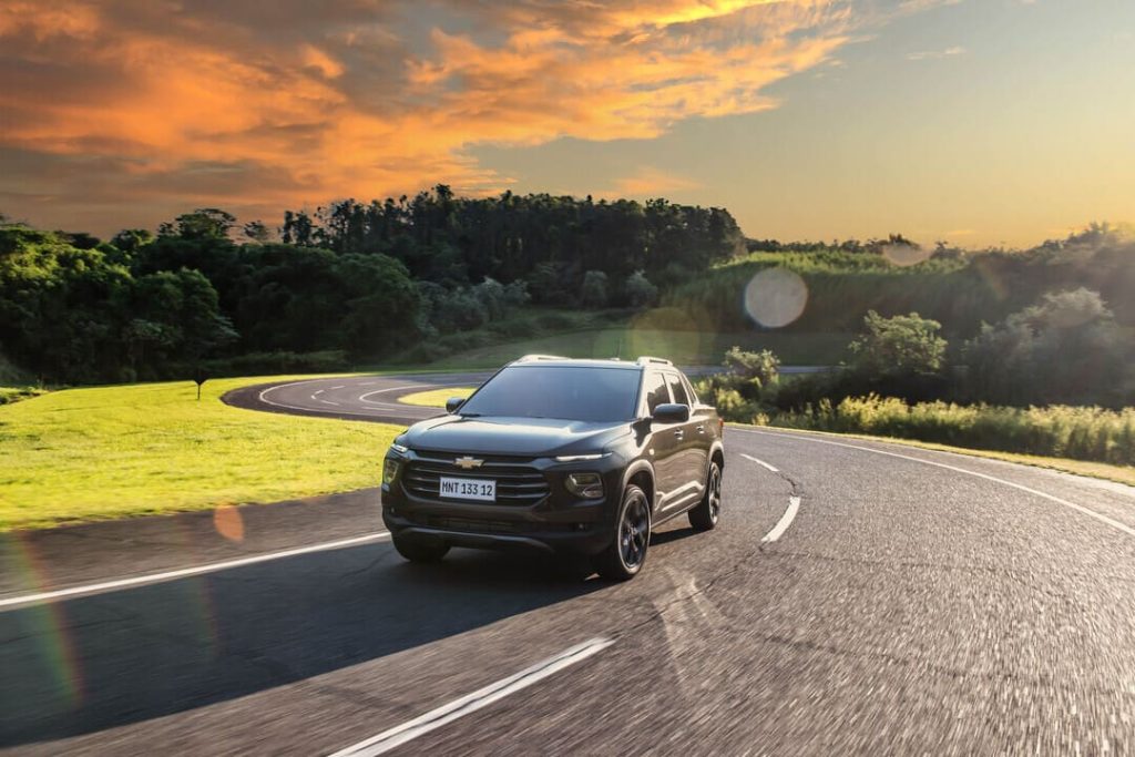 Carro preto em movimento em estrada curva com cenário natural ao entardecer, simbolizando segurança e direção defensiva.