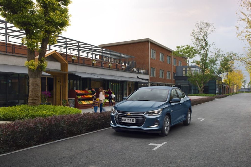 Carro azul parado em rua urbana sinalizada, próximo a pedestres e comércio, representando a importância da direção defensiva em áreas com circulação de pessoas.