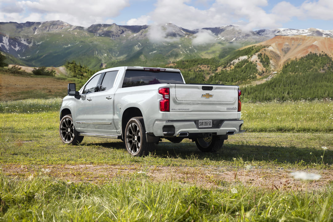 Picape Chevrolet Silverado prata estacionada em um campo gramado, com montanhas ao fundo.