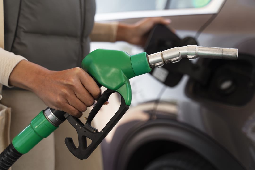 Pessoa abastecendo um carro com uma bomba de combustível de bico verde, indicando gasolina.