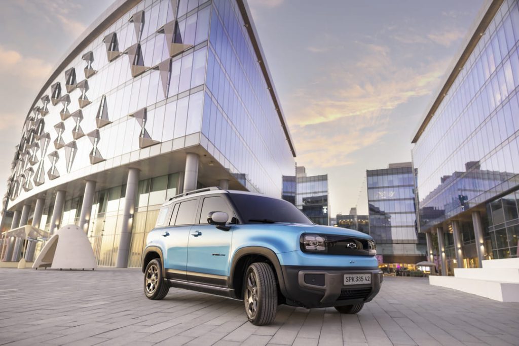SUV compacto azul metálico estacionado em frente a prédios modernos de vidro ao pôr do sol, representando carros com direção elétrica e hidráulica.