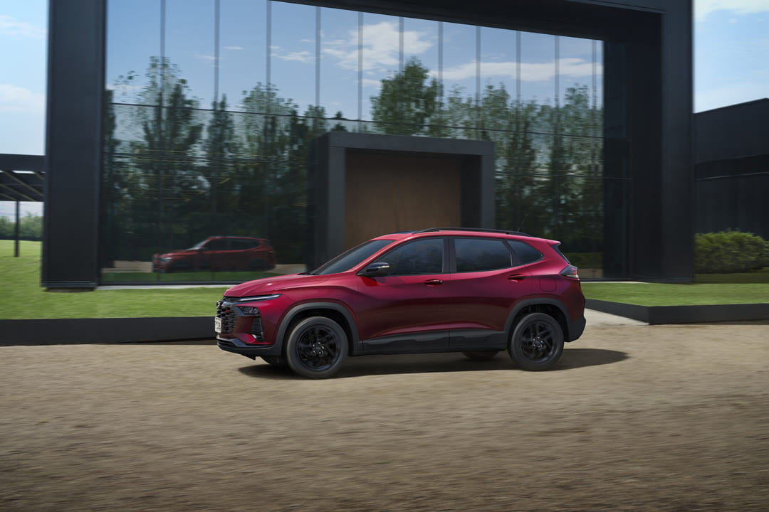 SUV vermelho metálico estacionado em frente a um prédio moderno com fachada de vidro, refletindo a paisagem ao redor.