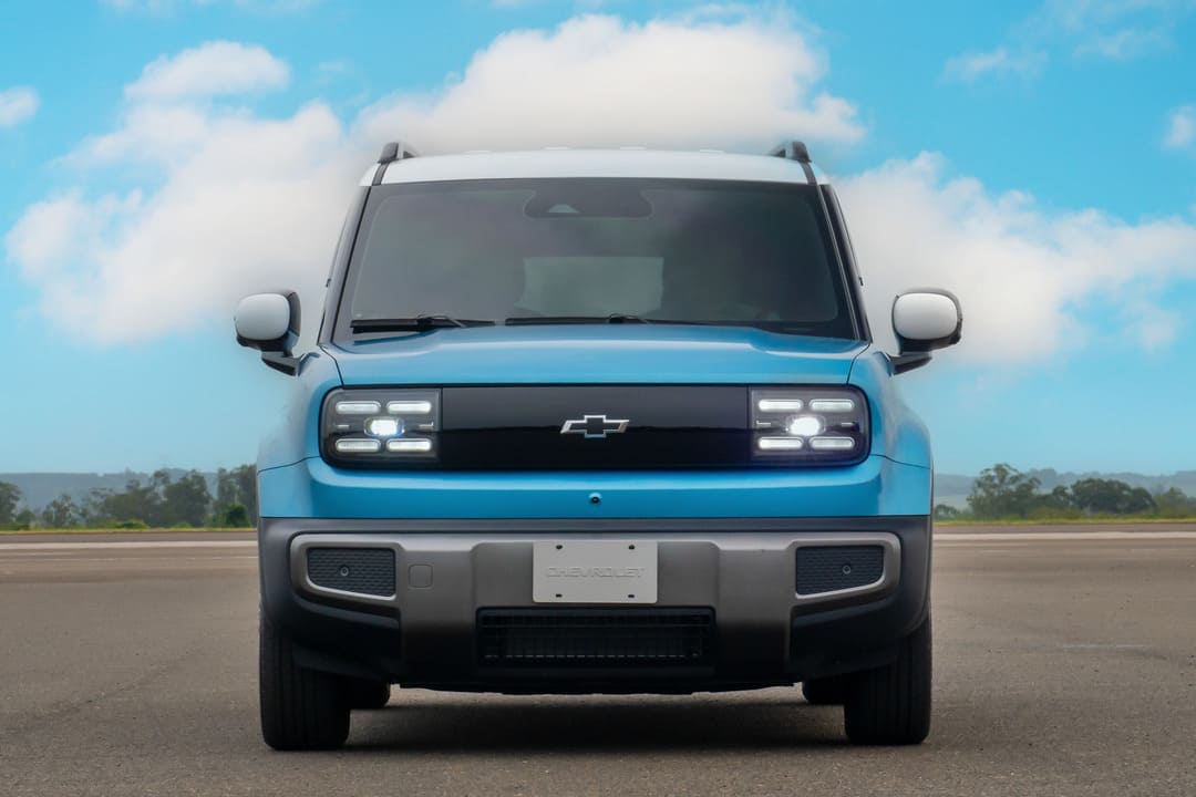 Vista frontal de um Chevrolet SUV compacto elétrico azul, com faróis de LED acesos, estacionado em pista asfaltada.