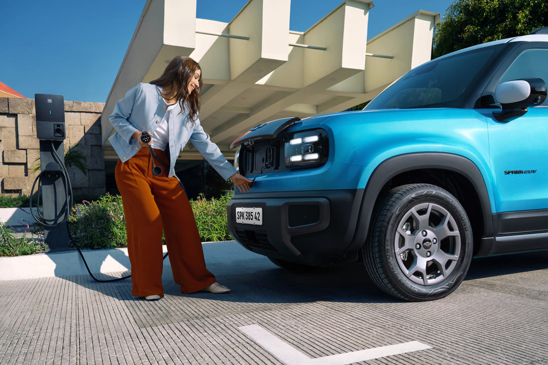 Mulher jovem carregando carro elétrico Chevrolet azul em estação de recarga, representando praticidade e tecnologia para novos motoristas.