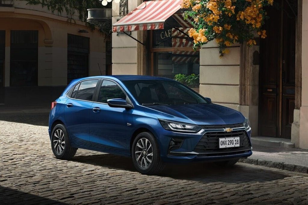 Carro Chevrolet azul estacionado em rua de paralelepípedos em frente a um café, ilustrando as opções de aquisição por meio de financiamento e consórcio Chevrolet.