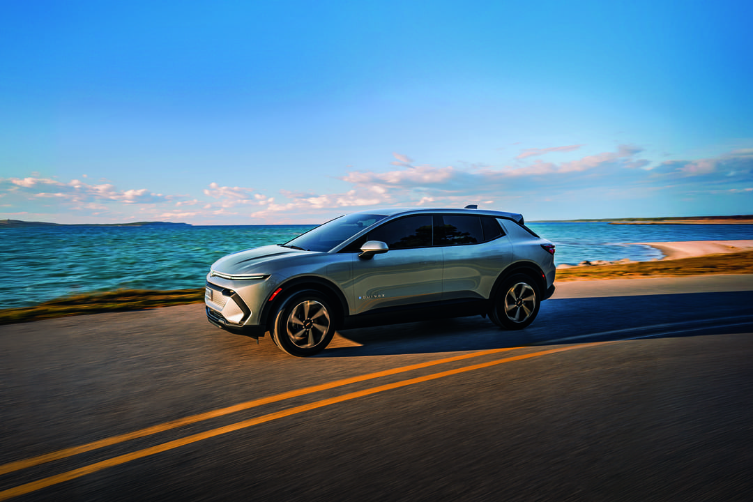 SUV elétrico da Chevrolet rodando em uma estrada costeira ao pôr do sol, simbolizando tecnologia avançada e mobilidade sustentável.